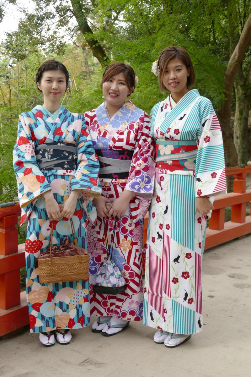 Czerwony mostek w świątynnym parku i trzy japońskie gracje w świątecznych kimonach